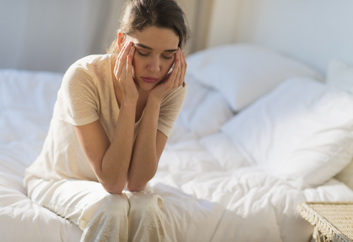 USA, New Jersey, Jersey City, Young woman sitting on bed with headache