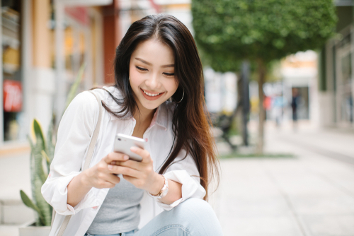 Smiling,Woman,Using,Mobile,Phone,On,The,Street