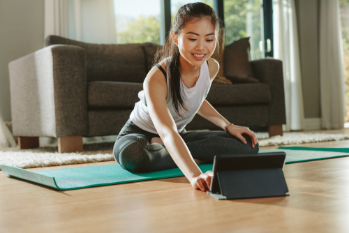 Smiling,Woman,Sitting,Exercise,Mat,And,Watching,Training,Videos,On