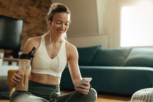 Happy,Sportswoman,Using,Smart,Phone,While,Drinking,Protein,Shake,After