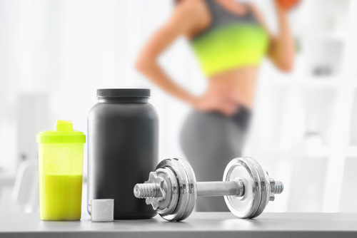 Composition,With,Metal,Dumbbell,,Protein,Shake,And,Blurred,Woman,On
