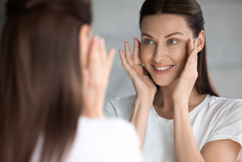 Attractive,Smiling,Young,Brunette,Woman,Looking,At,Mirror,,Touching,Face.
