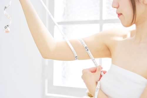 Asian,Woman,Measuring,Her,Upper,Arm,With,A,Measuring,Tape