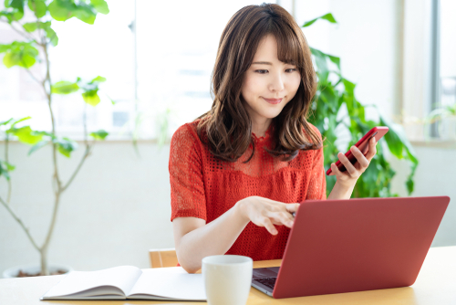Attractive,Asian,Woman,Using,A,Laptop,Pc,And,A,Smart